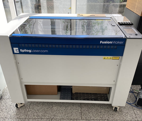 Epilog Fusion Maker 36 Maschine in Blau und Weiß mit Schneidtisch, Glasdeckel, Touchscreen und Rollen am Boden.