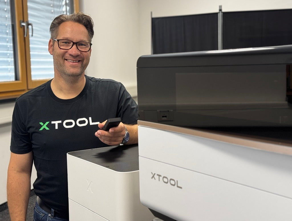 Ein Mitarbeiter von cameo Laser steht lächelnd neben einer xTool-Lasermaschine.